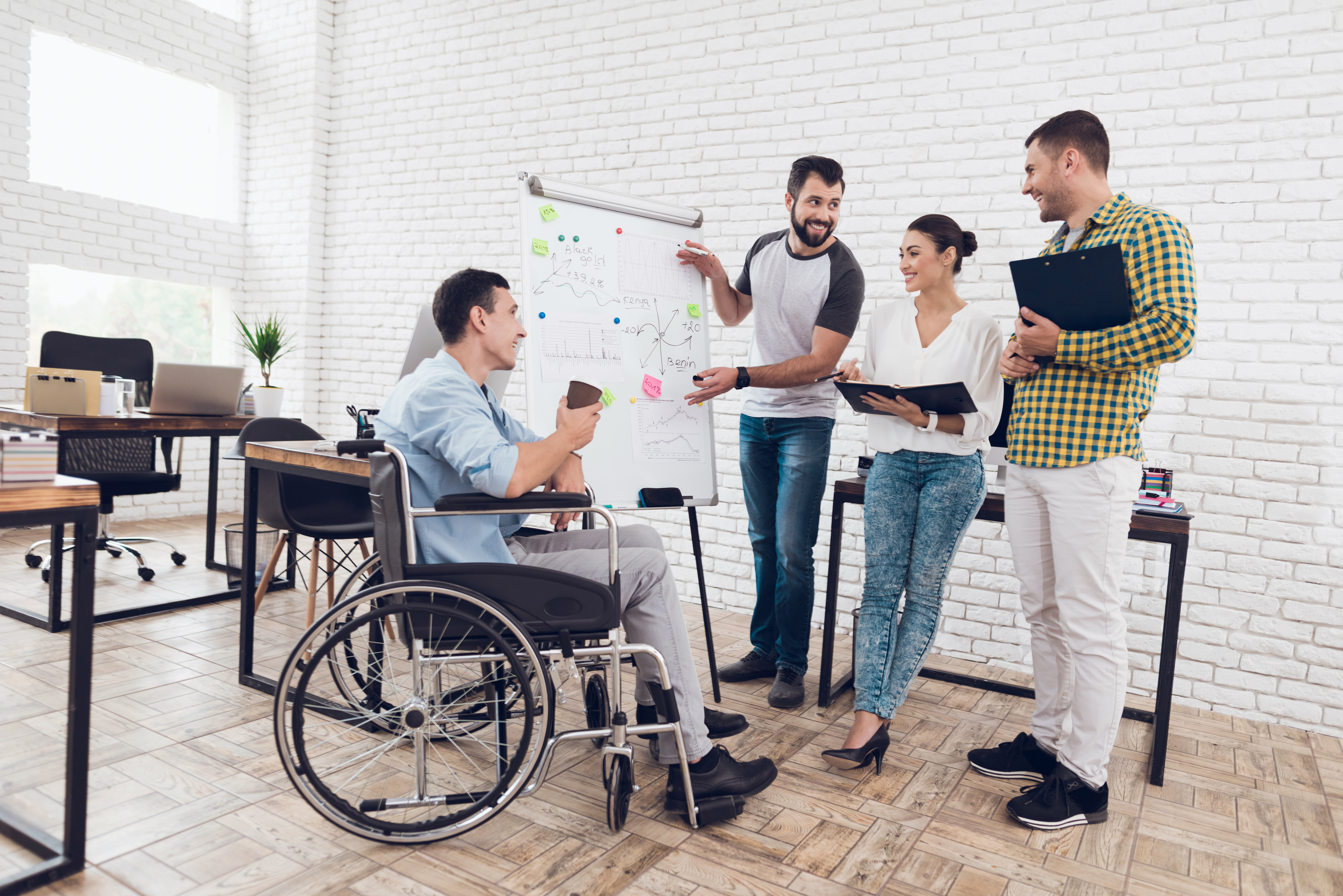 Photo showing a team of office employees including a man with disability using a wheelchair discussing work issues