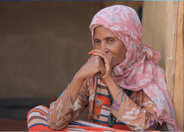 Old woman seated gazing away with hands crossed in front of her face