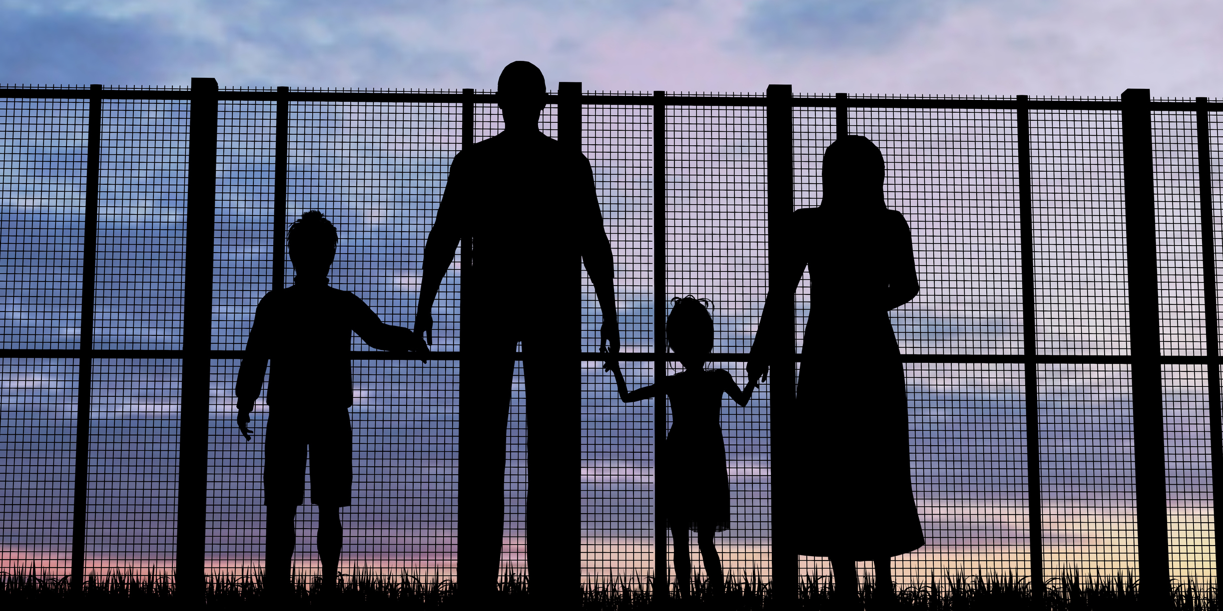 The back of four refugees facing a fence