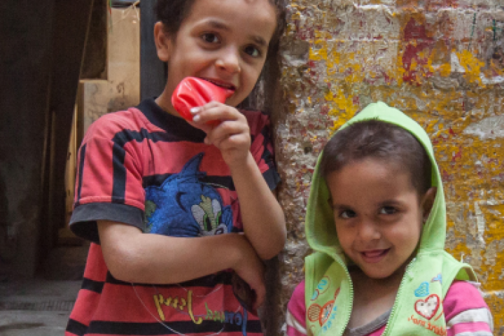 Two kids with a frail smile standing in a poor outdoor setting 