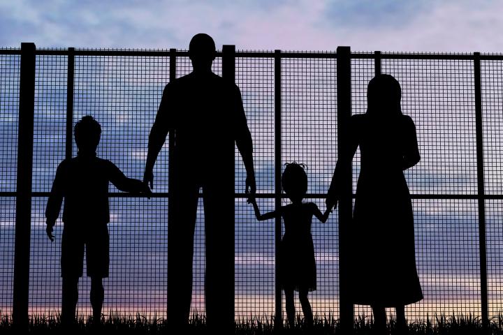 The back of four refugees facing a fence