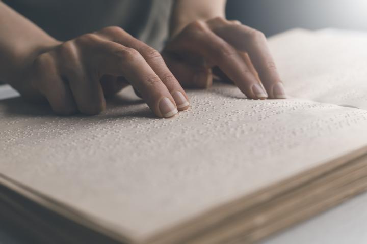 The hand of a blind man reads the text of a braille book