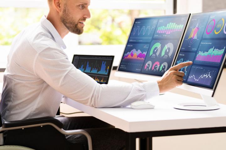 istock image: disabled man behind computer screens with statistics charts