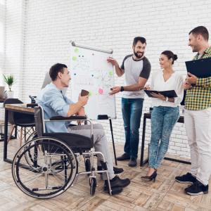 Photo showing a team of office employees including a man with disability using a wheelchair discussing work issues